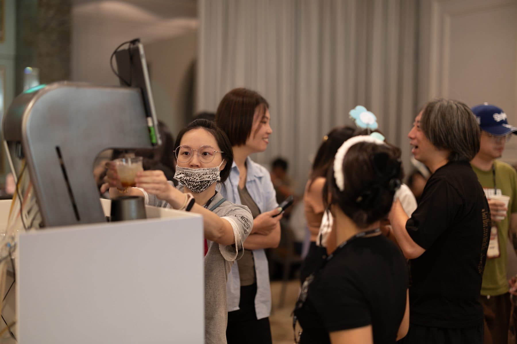 賓客從點點酒智能調酒機取走剛完成的飲品，旁邊還有其他賓客在等候