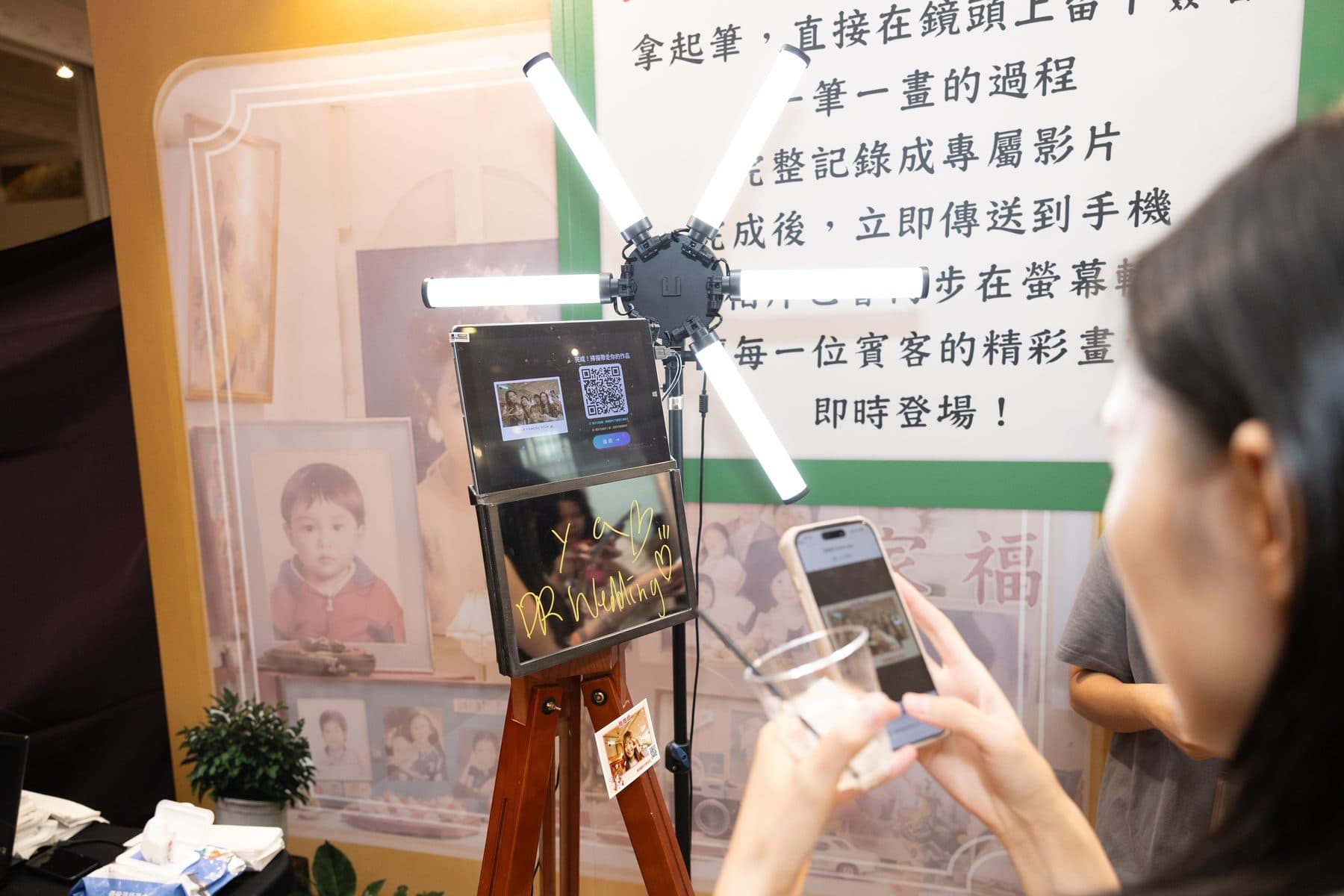 機台全景,賓客以手機掃描螢幕上的 QR Code,下方掛著已印出的照片